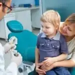 Little boy sitting with his mother on dental chair talking with dentist